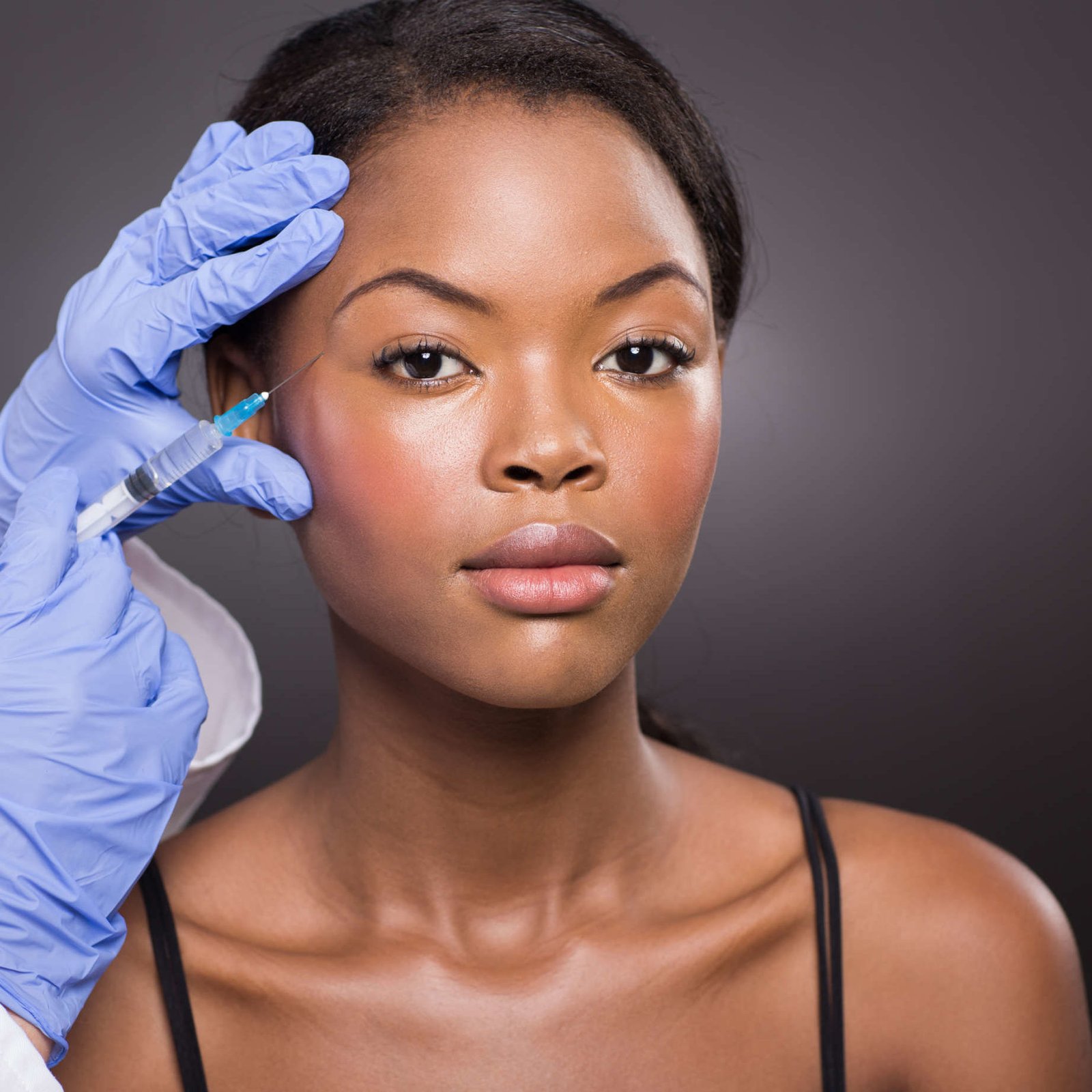 cosmetic surgeon injecting african american girl face on black background